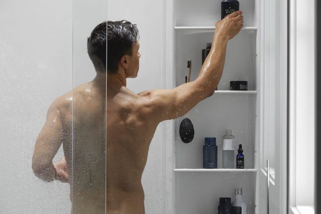 man reaching for shampoo bottle