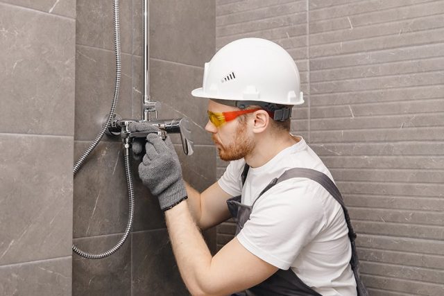 A man in a white hard hat and goggles installing shower fixtures in a home