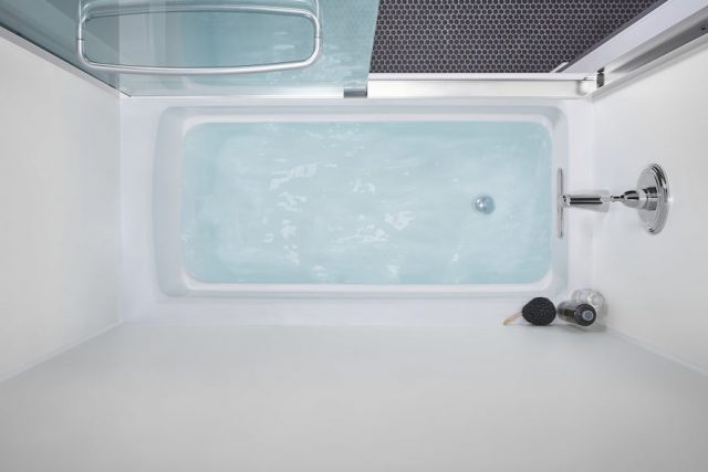 White bathtub with blue water and shower glass door
