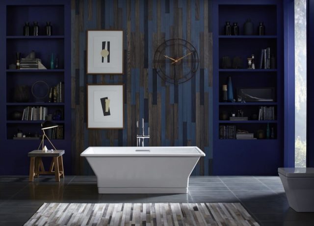 Dark blue bathroom with freestanding tub and wall hangings and shelving.