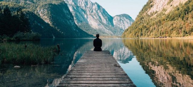 person sitting on a pier with the lake and mountains in view'