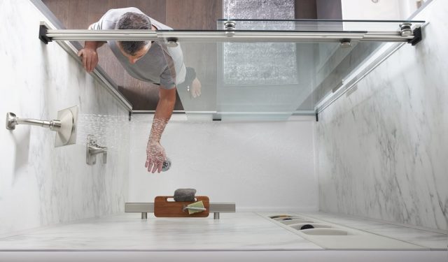 Person reaching into shower with water running to test temperature'